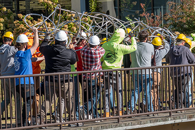 Students carry art installation across courtyard bridge