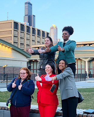 Members of the speech team pose outdoors with thumbs up.