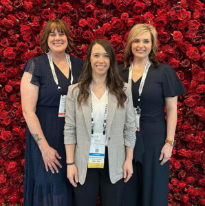 Cathrine Hoekstra, Kaylee Smith, and Emily Monti pose together in front of floral background