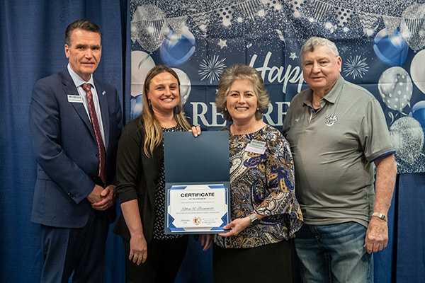Retiring Executive Assistant I Robyn Brummett with certificate standing next to JALC College President Dr. Kirk Overstreet, board member Jake Rendleman, and Assistant Vice President of Human Resources Stephanie Harner.