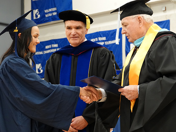 JALC Board member Jake Rendleman shakes hands with graduating student next to JALC College President Dr. Kirk Overstreet.