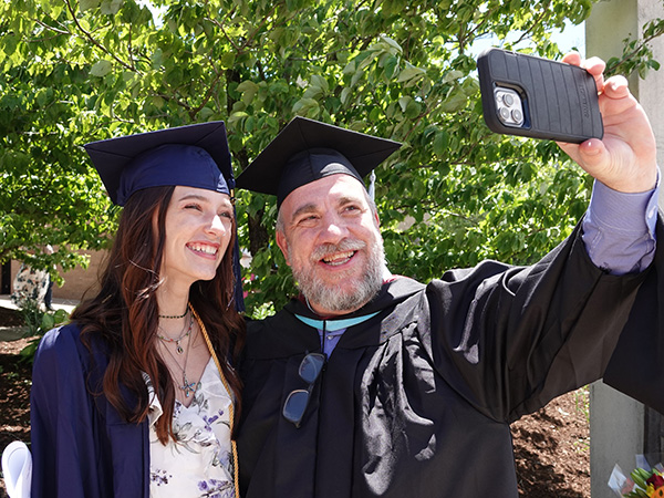 Instructor of Media Arts & Digital Media Technology Devin Miller poses for a selfie with student graduate outside of JALC.