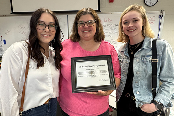 Nursing Instructor Crystal Young holding her scholarship document alongside two students.