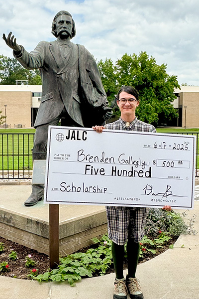 Brendan Gallegly stands next to John A. Logan statue holding up a check for a scholarship to John A. Logan College.
