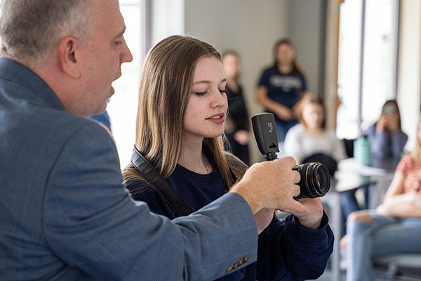 JALC Instructor of Media Arts, Devin Miller, shows student how to operate camera, while other students watch.