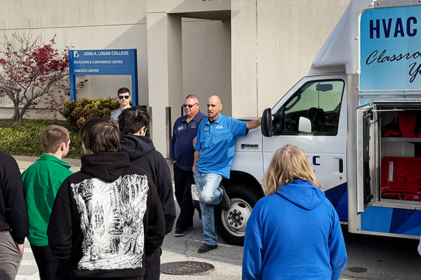 JALC Professor of Heating and Air Conditioning, Jason Stutes, speaks to students while leaning on the HVAC training vehicle.