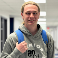 JALC Student Chandler Phemister stands in the hallway smiling and holding his backpack.