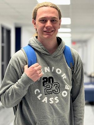 JALC Student Chandler Phemister stands in the hallway smiling and holding his backpack.
