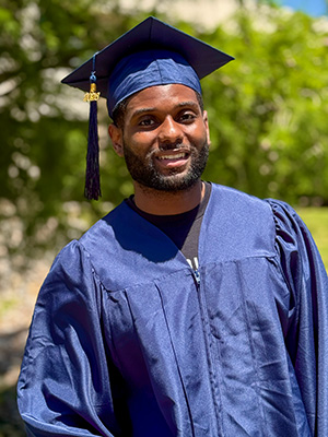 Dion Beals standing outdoors wearing graduation regalia.