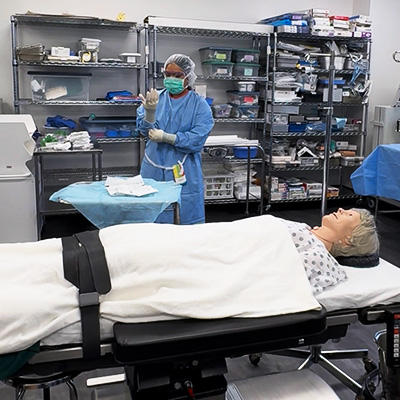 Student in medical clothing with manikin on stretcher in JALC lab.