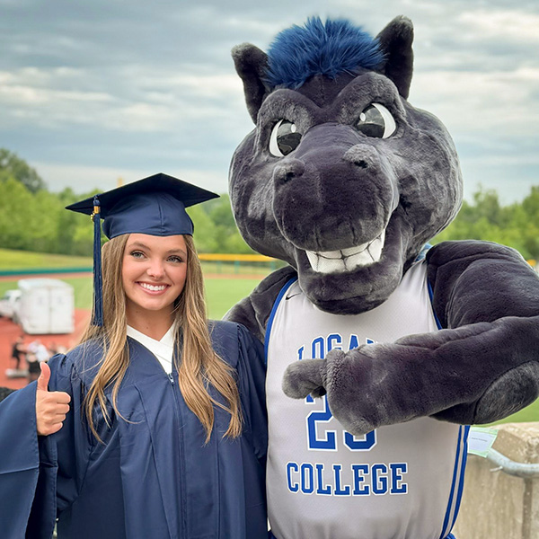 Student in graduation cap and gown posing with JALC Mascot Charger.