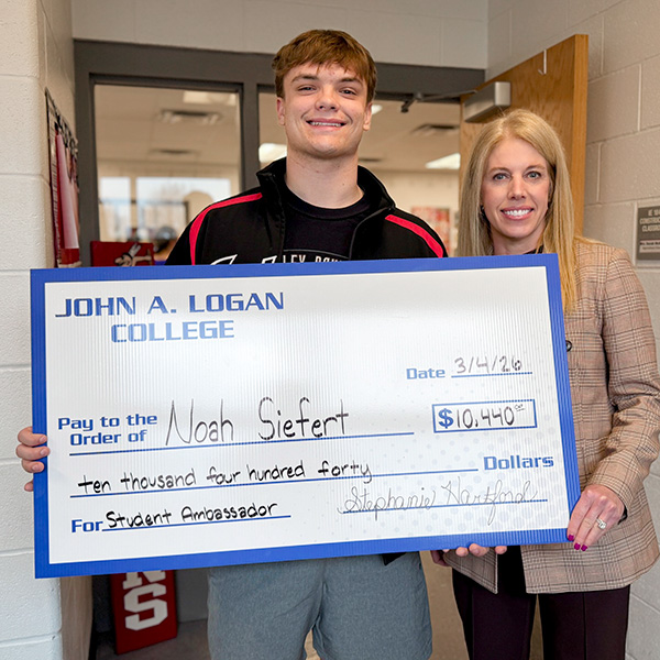 Noah Siefert holds Student Ambassador scholarship check while standing next to JALC Provost Stephanie Hartford.