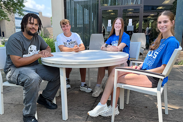 A group of student ambassadors sit at a table together in the JALC courtyard.