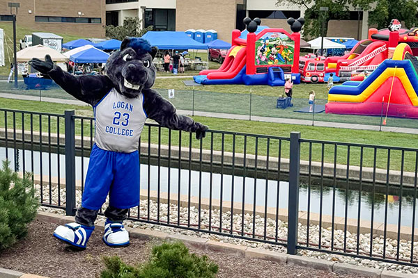 JALC mascot Charger next to fence with Southern Illinois Hunting and Fishing Days activities behind him.