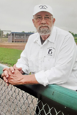 Dwight Hoffard standing, resting his arms on the fence at the John A. Logan College baseball fields.