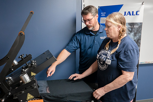 JALC Instructor of Digital Media Technology Brandon Johnson works with student on t-shirt print.
